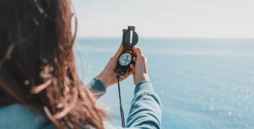 Frau mit Kompass aufs Meer blickend